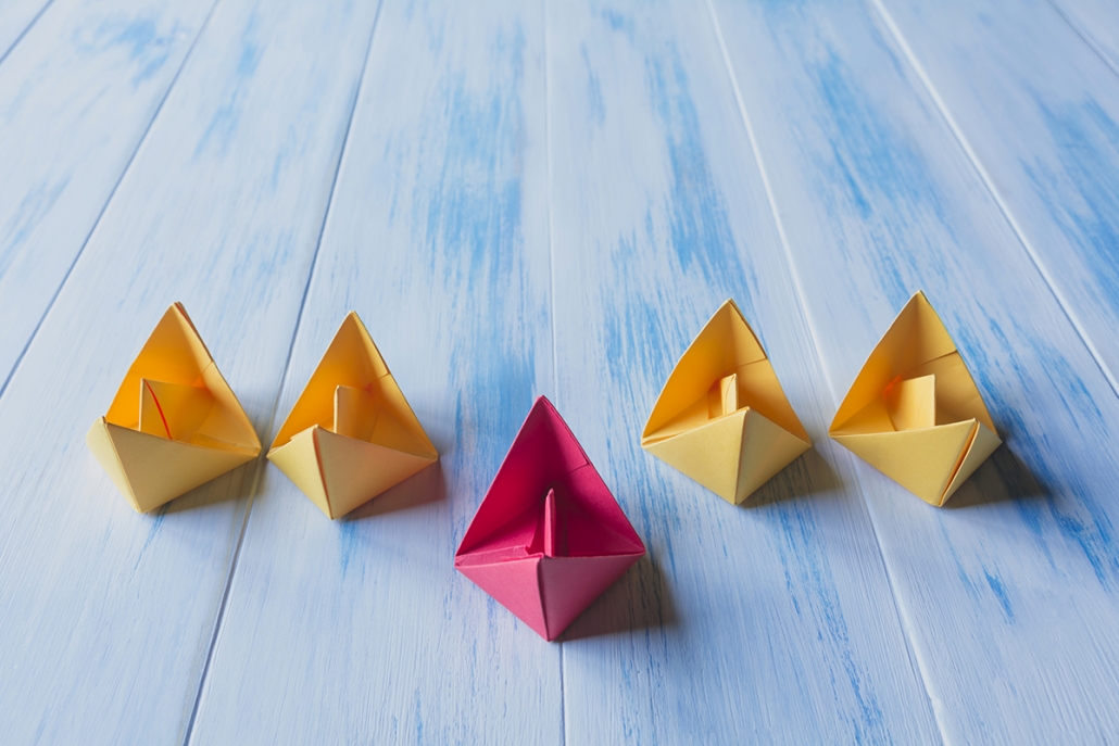Image of paper boats in a row with one standing in front of the rest