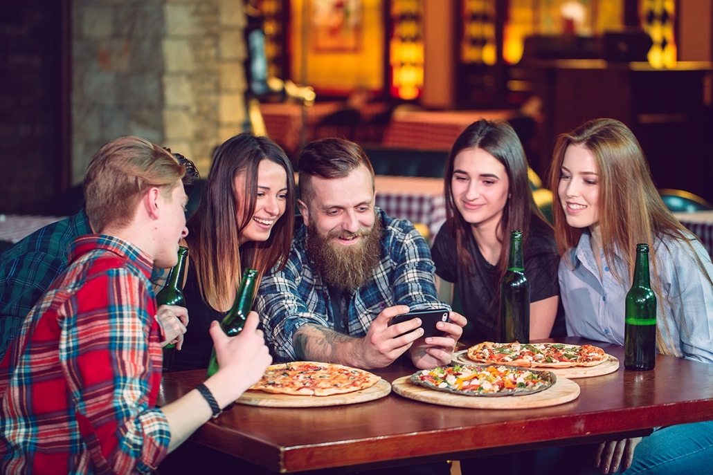 Young men and women gathering around looking at a cell phone - customer engagement marketing